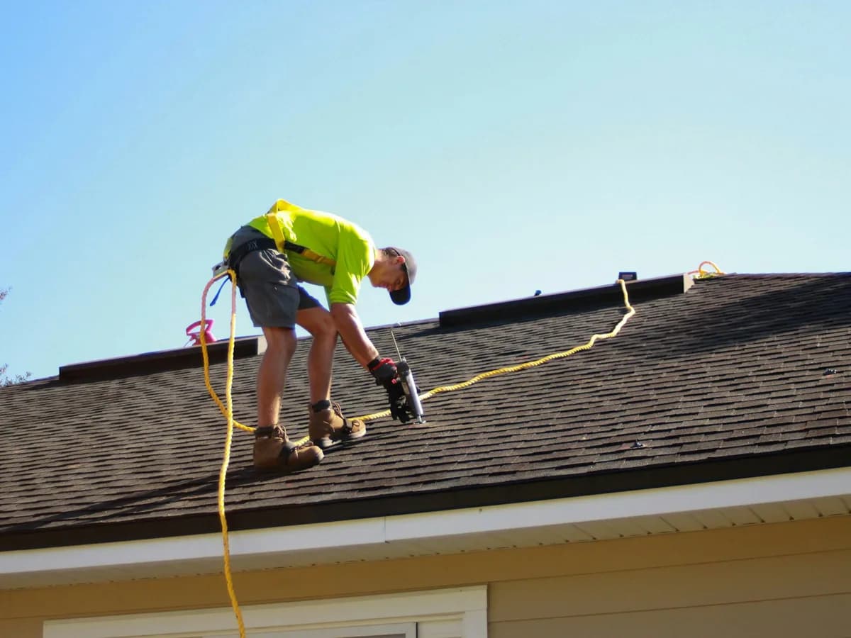 A roofer fastening shingles on a residential roof